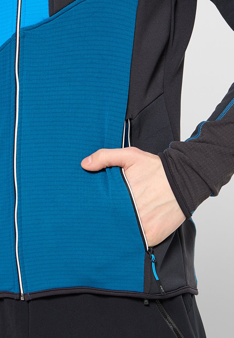 Chaqueta ajustada con un panel texturizado azul y mangas negras, con un bolsillo con cremallera y un detalle de ribete blanco en contraste.