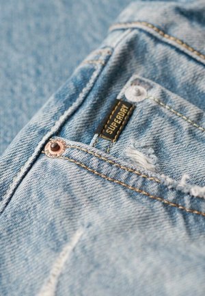 Jeans in denim blu chiaro con texture distressed, rivetti in rame, cuciture a vista e un'etichetta nera del marchio Superdry.