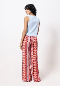 Hellblaues ärmelloses Oberteil, kombiniert mit weit geschnittenen Hosen, die ein farbenfrohes geometrisches Muster in Pink, Rot und Schwarz aufweisen.