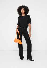 Tricou negru oversize, blugi negri cu talie înaltă și pantofi cu toc negri. Geanta portocalie are un design curbat. Texturi netede pe tot ansamblul.