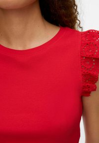 Rode kortemouwen top met geribbelde textuur en kantdetails op de mouwen. Ronde halslijn, slim fit ontwerp en levendige kleur.