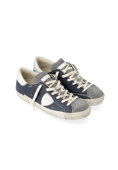 Et par slidte low-top sneakers med marineblå og grå ruskind, hvid læderhæl, hvide snørebånd og tykke hvide gummisåler på en hvid baggrund.