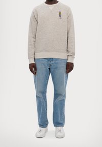 Gray sweatshirt with embroidered "Polo" logo, light blue denim jeans, and white sneakers. Relaxed fit, ribbed cuffs and hem.