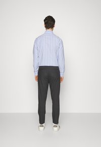 Błękitna koszula w paski z długimi rękawami, zestawiona z ciemnymi spodniami. Koszula ma klasyczny kołnierzyk i mankiety na guziki. Białe trampki z akcentami.