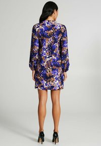 Fioletowa sukienka w kwiatowy wzór z długimi rękawami, dopasowanym krojem i krótkim dołem. Wykonana z gładkiej tkaniny o błyszczącym wykończeniu. Czarne szpilki.