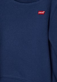 Sudadera azul marino hecha de tela suave, con cuello redondo y un pequeño parche con el logo rojo de Levi's en el área del pecho izquierdo.