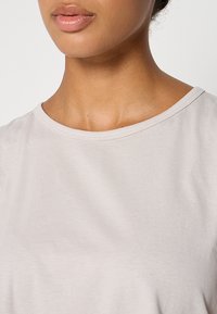 Jasnoszary t-shirt z krótkim rękawem, o okrągłym dekolcie i gładkiej fakturze, z detalami szycia wzdłuż kołnierza.