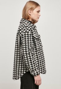 Houndstooth-mønstret, overdimensjonert sort og hvit jakke i myk, teksturert stoff med krage og forlommer, stylet med en avrundet kant.