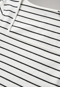 Tela blanca con finas rayas horizontales negras uniformemente espaciadas y escote cuadrado. Etiqueta visible "Made in Bangladesh".