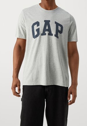 Maglietta di cotone grigia con la scritta "GAP" stampata in lettere maiuscole blu scuro sul petto. Presenta un collo a giro e maniche corte.