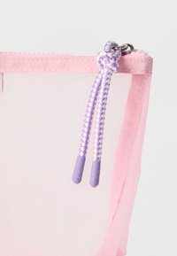 Κοντινό πλάνο ροζ τσαντάκι με φερμουάρ από δίχτυ και μοβ-άσπρο πλεγμένο κορδόνι συνδεδεμένο στο τρέιλερ του φερμουάρ.