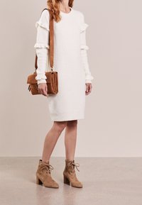 Biała dzianinowa sukienka z falbankowymi rękawami, zestawiona z brązową zamszową torebką na ramię i beżowymi botkami z wiązaniem na kostkę i obcasem w kształcie bloku.