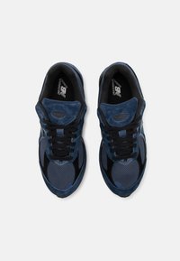 Zapatillas deportivas azul marino realizadas en ante y malla, con una suela texturizada negra, cordones negros y un logotipo en la lengüeta y la plantilla.