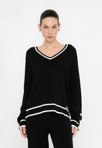 Zwarte v-hals trui met witte gestreepte accenten, ontspannen pasvorm, geribde boorden en zoom, met gouden knoopdetails op de mouwen.