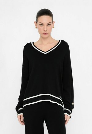Pullover en v noir avec des accents rayés blancs, coupe décontractée, manches et ourlet côtelés, avec des détails de boutons dorés sur les manches.
