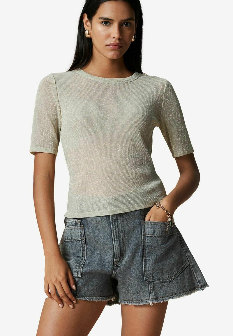 Lys beige, kortærmet striktrøje med en subtil glans, parret med højtaljede grå denimshorts med frayed kanter og lommer.