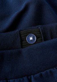 Námornícky modrý tkanina s prúžkovaným pásom v páse, s priehľadným plastovým gombíkom a čiernymi elastickými vložkami pre nastaviteľnosť. Textúrovaný bavlnený zmes.