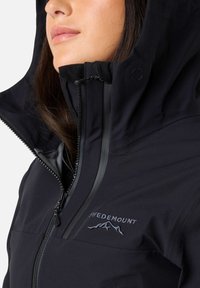 Sort udendørsjakke med lynlås foran og hætte. Har en blød indvendig foret og detaljeret logo broderi på brystet.
