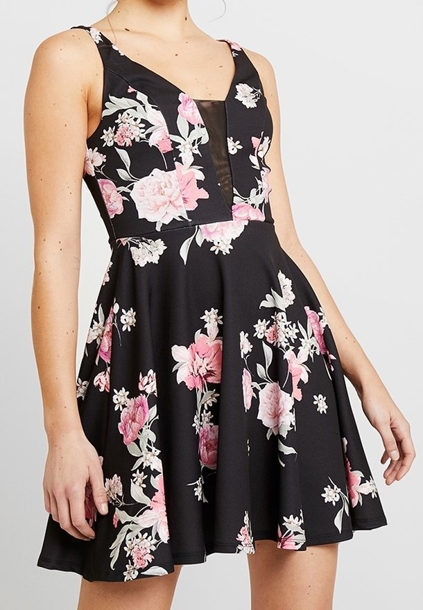 Femme portant une robe noire sans manches avec des motifs floraux roses et blancs et un décolleté en V profond avec une incrustation noire transparente.