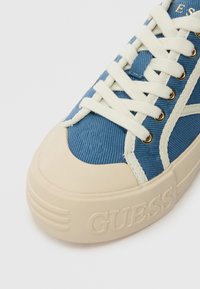 Plave platnene tenisice s bijelim vezicama, krem gumeni potplat i zlatni rupici. Sadrži riječ "GUESS" uvučenu sa strane.