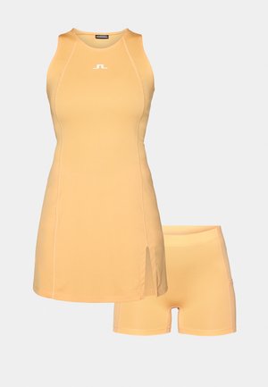 Žuta atletska haljina s prilagođenim gornjim dijelom i bočnim prorezima, uparenim s odgovarajućim šortsevima. Napravljena od glatkog, rastezljivog materijala s minimalnim šavovima.