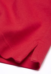 Tissu rouge tissé avec une surface texturée, présentant un bord plié et une petite fente latérale. Matière souple et douce.