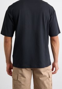 Černé bavlněné tričko s volným střihem a krátkými rukávy, s jednoduchým zadním dílem a kruhovým výstřihem, doplněné béžovými cargo kalhotami.