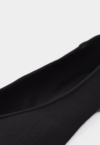 Μαύρο παπούτσι slip-on με διακριτό μοτίβο διαμαντιού και στρογγυλεμένη άκρη, αποτυπωμένο σε λευκό φόντο.