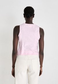 Top sem mangas em linho rosa, com decote redondo, design cropped e tecido texturizado. Usado com calças brancas de cintura alta e pernas largas.