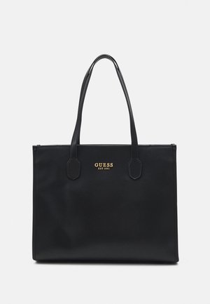 Sort rektangulær lædertaske med to håndtag og guld "GUESS EST 1981" logo på frontens midte.