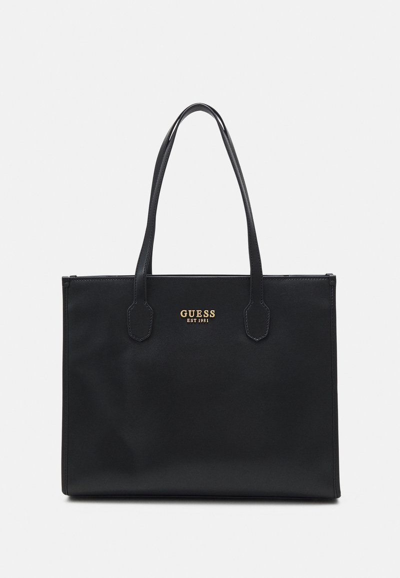Sac cabas rectangulaire en cuir noir avec deux anses et logo doré "GUESS EST 1981" au centre avant.