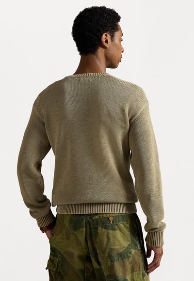 Khakiwełniany sweter z ribbami na mankietach i dolnym brzegu, w połączeniu z zielonymi spodniami w kamuflaż. Posiada luźny krój i teksturowany materiał.
