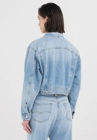 Lyseblå, kort denimjakke med klassisk krage, lange ermer og knappe-detaljer på mansjettene. Har en svakt falmet tekstur.