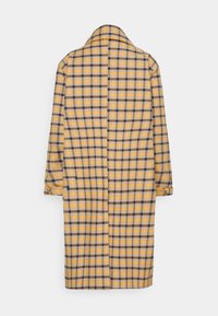Żółto-szary płaszcz w kratę z długim krojem, szerokim kołnierzem i podwijanymi rękawami. Widok z tyłu pokazuje zapinanie na guziki i szwy.