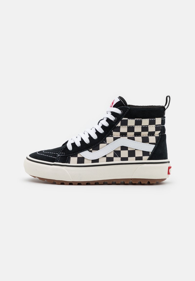 Sneaker montante à motif damier noir et blanc avec dessus en suède et textile, lacets blancs et semelle en caoutchouc beige. Accent rouge sur le talon.