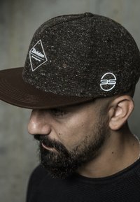 Brown cap made of textured fabric with a dark brim, featuring a white diamond logo and a circular logo on the side.