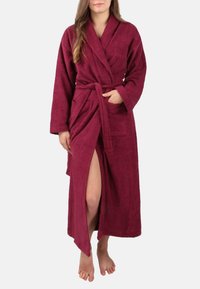 Bordeauxfarbener Frottee-Bademantel mit langen Ärmeln, Taillenschnürung und Fronttaschen. Besitzt einen schulterhohen Schlitz auf der linken Seite und eine weiche Textur.