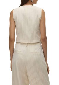 Haut sans manches de couleur crème avec des rayures verticales. Coupe courte, tissu lisse, silhouette slim, assorti à un pantalon à rayures similaires.