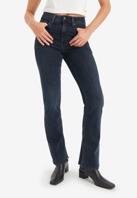 Mörkblå, högmidjade raka jeans med en något utsvängd ben och sidofickor vid fållen, i kombination med svarta klackade ankelstövlar.