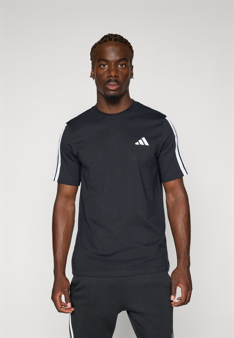 Zwarte t-shirt met korte mouwen, voorzien van een wit drie-strepen ontwerp op de schouders en het Adidas-logo op de linkerkant van de borst. Van katoen.