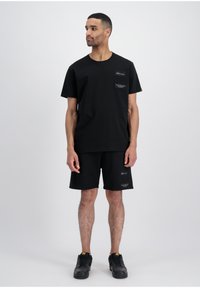 Černý bavlněný set trička a šortek se dvěma náprsními kapsami s kontrastními štítky. Nosí se s černými sportovními botami.
