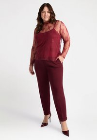 Burgundy spets långärmad topp lager på en ärmlös skjorta, parat med matchande smala byxor och spetsiga högklackade skor. Slät tygfinish.