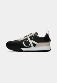 Svart sneaker med en beige semsket aksent, hvit logo, gummisåle og snører. Har et slitesterkt overmateriale og en løfletapp på hælen.
