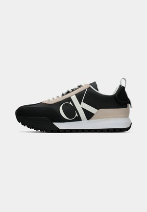 Schwarzer Sneaker mit beigem Wildleder-Akzent, weißem Logo, Gummisohle und Schnürsenkeln. Verfügt über ein strapazierfähiges Obermaterial und eine Zuglasche an der Ferse.