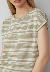 Zielona i kremowa, w pasy, koszulka z krótkim rękawem, z okrągłym dekoltem i miękkim, teksturowanym materiałem. Subtelne różnice w szerokości pasków.