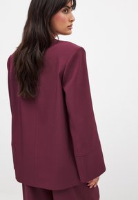 Bordo bleiser, mille serve, pikad varrukad ja sile tekstuur. Omab puhtaid jooni ja minimalistlikku disaini.