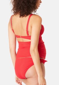 Maillot de bain deux pièces rouge avec un haut ajusté aux bretelles réglables et une texture froncée, associé à un bas taille haute.
