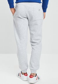 Pantalones de chándal grises con un diseño entallado, hechos de tejido suave, con un bolsillo trasero y un puño acanalado. Combinados con zapatillas blancas.