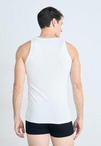Débardeur en tissu blanc avec de larges bretelles, coupe ajustée et texture lisse, associé à un short noir, vu de dos.