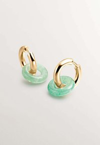 Pendientes de aro en tono dorado con acentos circulares translúcidos de color verde claro. El metal liso y la piedra texturizada crean acabados contrastantes.